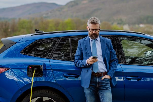 A person leaning against the side of their blue leased business car while it charges.